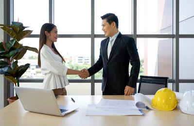 asian project owner in suit and his business partner shaking hands after checking the construction drawing. morning work atmosphere in a modern office.