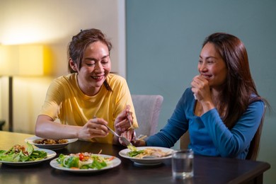 two asian woman friends having dinner eating pasta and salad with talking together at home. attractive female girlfriends relax and enjoy indoor lifestyle activity and holiday celebration together
