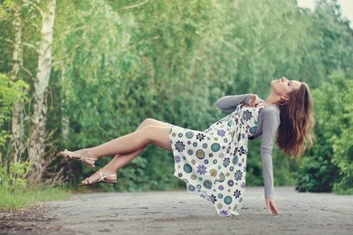 young brunette girl in colorful dress levitating in the park. green trees lit with bright summer sunlight.