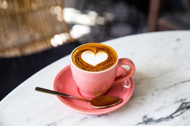 trendy pink cup of hot cappuccino on marble table background. heart shape latte art for symbol of love. one cup for morning routine.