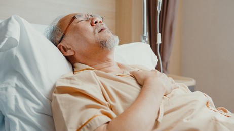 sad senior asia man having having heart attack lying on hospital bed and press emergency button. sick aged guy lying hospitalized in a medical clinic. health insurance or hospitality concept.