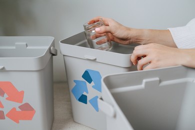 hands of a woman sorting garbage beween small recycle bins at home. they have differently colored arrows on them. holding a jar of glass.