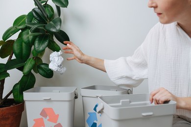 woman sorting garbage, throwing a piece of crampled paper in a small recycle bin at home. there are several of them, with differently colored arrows on them.