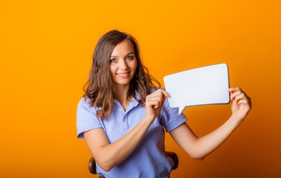 happy young woman holding empty speech bubble on yellow background.