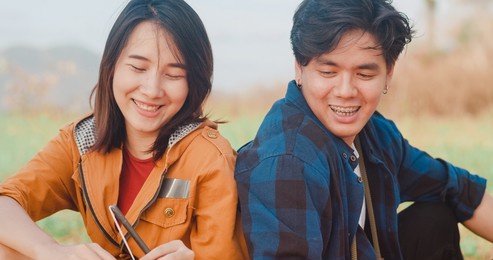 young asia campers couple sitting in chairs by tent near seaside. male and female traveler relaxing and talking on a summer day at campsite. outdoor activity, adventure travel, or holiday vacation.