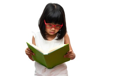 happy asian little preschool girl wearing red glasses holding and read a green book on white isolated background. concept of school kid and education in elementary and preschool, home school