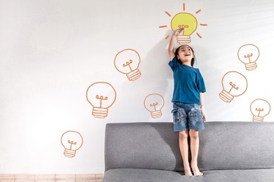 a smart asian little child girl standing against white wall background with drawing imagination light bulb ideas sign. girl power future dream and creativity concept idea. copy space and text.