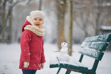 adorable toddler girl building a snowman on a day with heavy snowfall. happy child playing with snow. winter activities for kids
