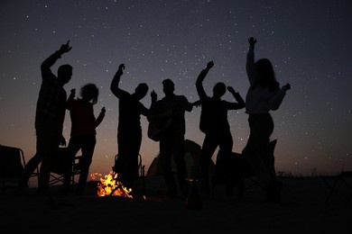 group of friends having party near bonfire in evening. camping season