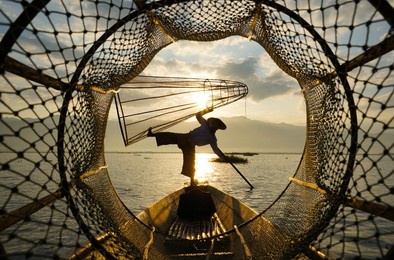 view through fish coop of local fisherman standing on boat in lake at sunrise
