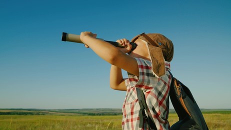 happy little boy child playing in park in an aviator's helmet looks through spyglass in summer on nature. kid son of traveler dreams, fantasies against blue sky on playground. leader winner, travel.