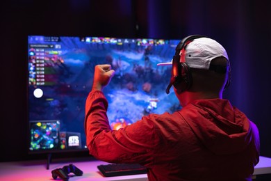rear view young player video computer pc. young man sitting on chair in game station.streamer man wearing headphone  playing action game online in the darkroom.
