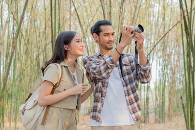 beautiful, happy asian young man,woman smile and look at camera after boyfriend take photo, picture of her while traveling together at forest, nation park. summer vacation outdoor with couple concept.