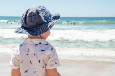 little boy wearing hat on a sandy ocean beach in australia. sun safety - sunscreen, hat and shirt. travel with kids