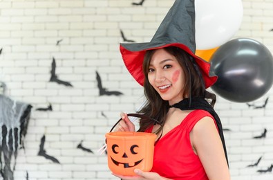portrait of beautiful young asian woman wearing witch costume posing with balloons on background decorated for halloween party - free space for copy text