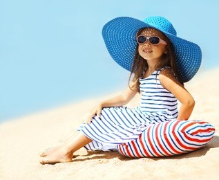 pretty little girl in a striped dress and hat relaxing on the beach near sea, summer, vacation, travel - concept