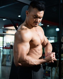 portrait shot of shirtless adult asian men show off his strong bicep and arm muscle inside of fitness gym. bodybuilding or professional athlete workout concep.t