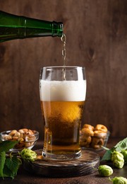 pouring of cold beer in glass with foam. beer and snacks on dark wooden table. vertical image