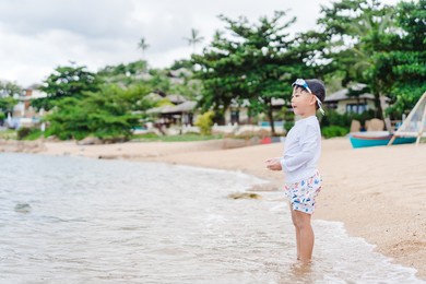 4 years old asian boy play on the rock on sea beach.vacation and relax.playful active kid on beach in summer vacation and child development.asian kid toddler boy play in sea sand beach in thailand.