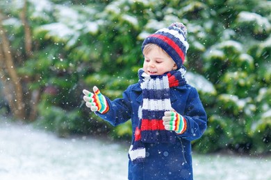 cute little funny child in colorful winter fashion clothes having fun and playing with snow, outdoors during snowfall. active outdoors leisure with children. kid boy and toddler catching snowflakes.