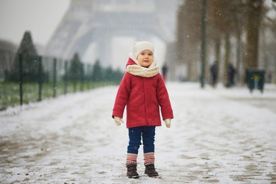 adorable toddler girl near the eiffel tower on a day with heavy snowfall in paris, france. happy child playing with snow. winter activities for kids
