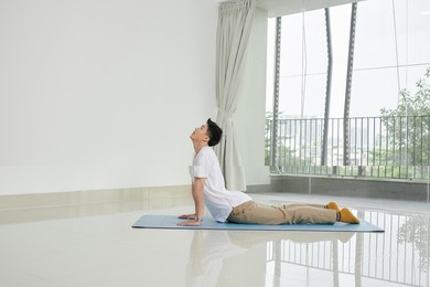 young asian man playing snake posture yoga on the yoga mat at home