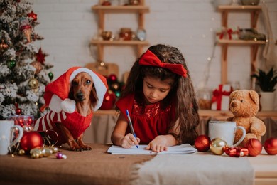 cute little girl with a a dwarf dachshund writes a letter with wishes to santa claus. winter new year's christmas concept. place for text. high quality photo