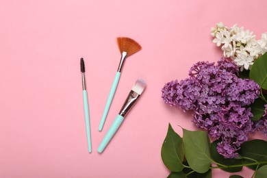 makeup brushes with branches of blooming lilacs on pink background. spring, beauty concept. top view. flat lay