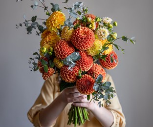 woman hid her face with a bouquet of yellow and orange chrysanthemums, gray background, copy space.