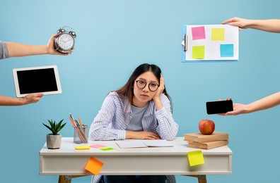 deadline and multitask concept. tired asian lady stressed by a lot of work, sitting at the desk over blue background and looking at camera. hands with tablet, watch, tasks and smartphone