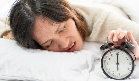 asian woman laying on the bed covered in blankets hearing the alarm clock felt lazy to wake up early on the bed in her bedroom in the house. 