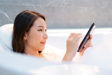 relaxed asian woman using the smartphone while bathing with foam in bathtub.