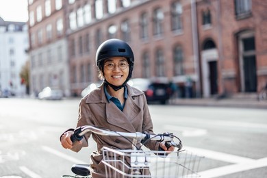 portrait of a smiling asian woman going to work on a bicycle. wearing a helmet and riding a bicycle in a bicycle lane.