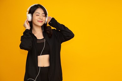 asian fitness woman listening music with headphone on smartphone isolated on yellow background