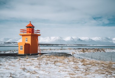 beautiful view of orange colored lighthouse on the northcoast of iceland, west iceland in winter season with volcanic rocks and brown grass on cloudy day.