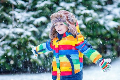 cute little funny child in colorful winter fashion clothes having fun and playing with snow, outdoors during snowfall. active outdoors leisure with children. kid boy and toddler catching snowflakes