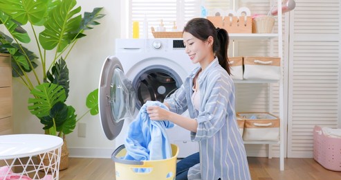 asian housewife put clothes into washing machine happily at home