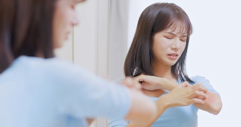 close up of asian woman has dry skin and scratches her arms in front of mirror at home