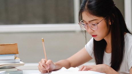 asian student women reading books in library at university. young undergraduate girl do homework, read textbook, study hard for knowledge and education on lecture desk at college campus.