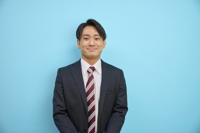 japanese man in a suit laughing refreshingly in front of a blue background