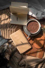 a cup of hot chocolate with cat, notebooks, cookies, leaves on wooden board and brown background, aesthetic concept