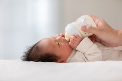 close up hand of mother holding milk bottle newborn baby lying on bed drinking milk.cute infant baby feeding milk with love at home.newborn concept