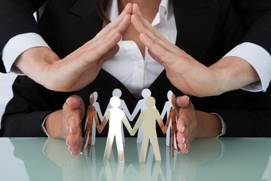 cropped image of young business people sheltering team of paper people at office desk