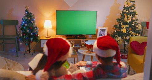 christmas holidays concept – asian young couple are watching green chroma key screen tv and petting their cat while sitting on couch in the living room