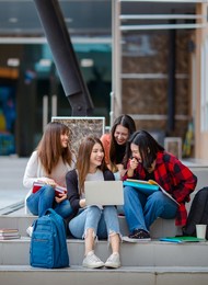 group of delighted asian female students gathering on stairs in university campus and doing homework together while using laptop. concept for close friend of teens life.