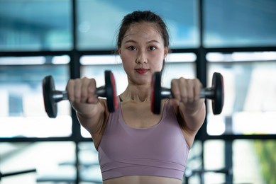 close up an asian woman raises a pair of dumbbells in front of her to build arm muscles