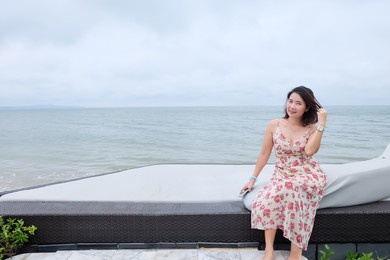 short-haired asian woman in pink dress sitting on a sunbed by the sea. summer vacation .