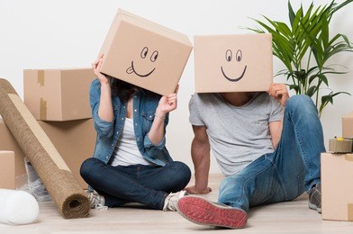 couple with cardboard boxes on their heads with smiley face sitting on floor after the moving house