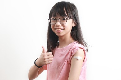 portrait of happy asian teenager girl get vaccinated, showing her shoulder with band-ais and thumb up after getting a vaccine, isolated on white background