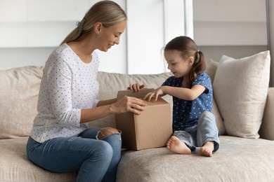 happy young mother unpacking cardboard box with interested cute little preschool kid daughter, feeling excited of getting parcel with wished purchase item from internet store, online shopping concept.